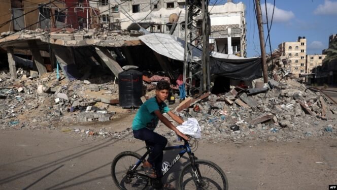 
 Seorang anak laki-laki Palestina menaiki sepeda melewati gedung-gedung yang hancur di Rafah, di selatan Jalur Gaza, pada 26 Mei 2024. (Foto: AFP/Eyad Baba)