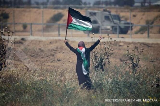 
 ILUSTRASI. Wanita yang memegang bendera Palestina di Pagar perbatasan Israel-Gaza, di selatan Jalur Gaza 15 Mei 2019.